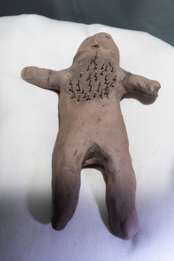 Brown clay form in the shape of a human body, willed with around 20 metal pins.