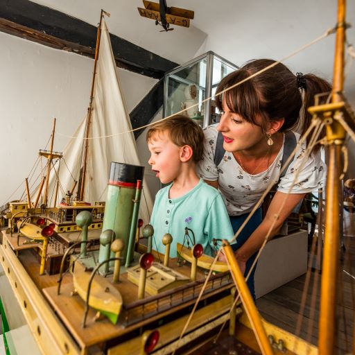A small child, with mother behind looks at a toy ship