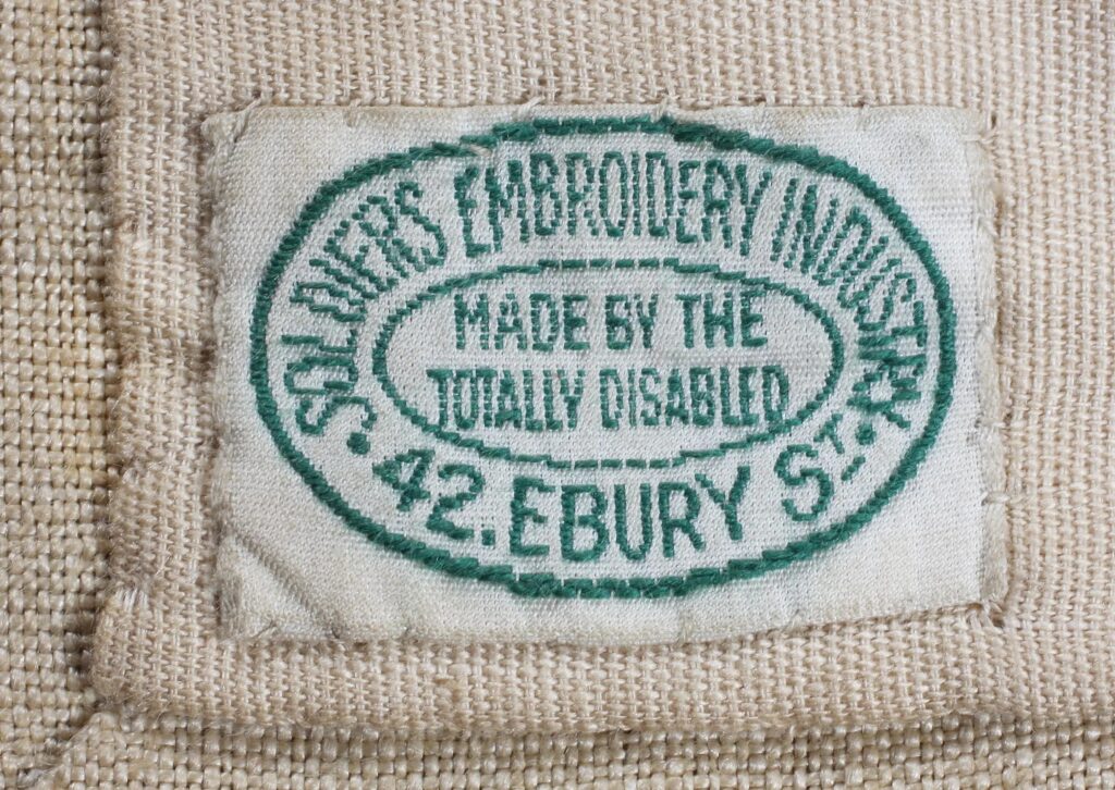 Cream label from a large embroidery. 'Soldiers Embroidery Industry, 42 Ebury St, Made by the totally disabled',