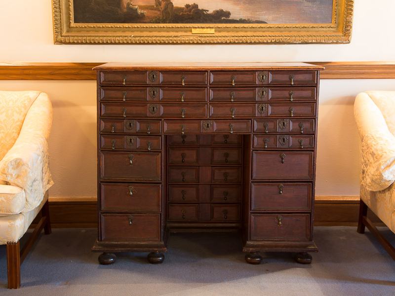Dark brown cabinet with 27 draws with teardrop handles. Cabinet is situated between two cream armchairs.
