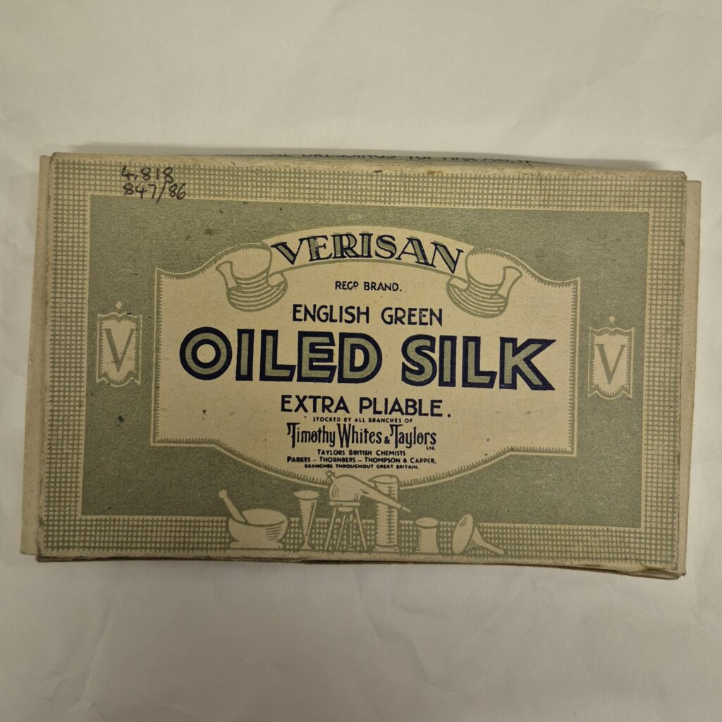 Flat cream rectangular packet with pale green illustrated design that includes scroll motifs and chemists' equipment. Text reads 'Verisan, English Green Oiled Silk'.