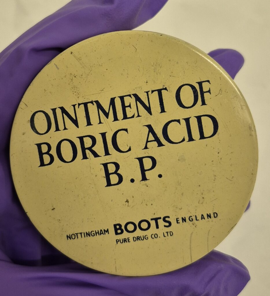Round cream tin with black text that reads 'Ointment of Boric Acid P.P. With the logo of Boots Nottingham England below.