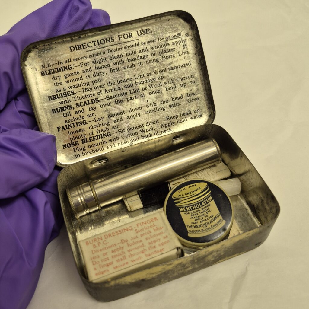 Metal rectangular tin, open to show contents. The lid has black text titled Directions for Use with paragraphs sub headed with different ailments. In the contents compartment there is a silver metal cylinder, a white card with red text and a small black tin with a cream illustration of a spool of thread.