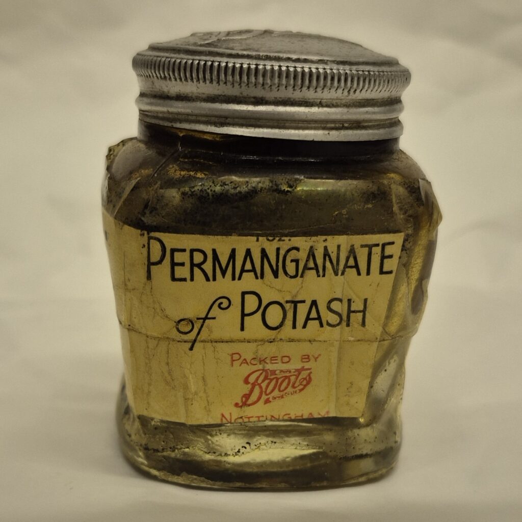 Square glass jar with metal lid. Cream label writes 'Permanganate of Potash' in black writing. Under this, it reads, 'packed by' above the Boots logo, both in red font.