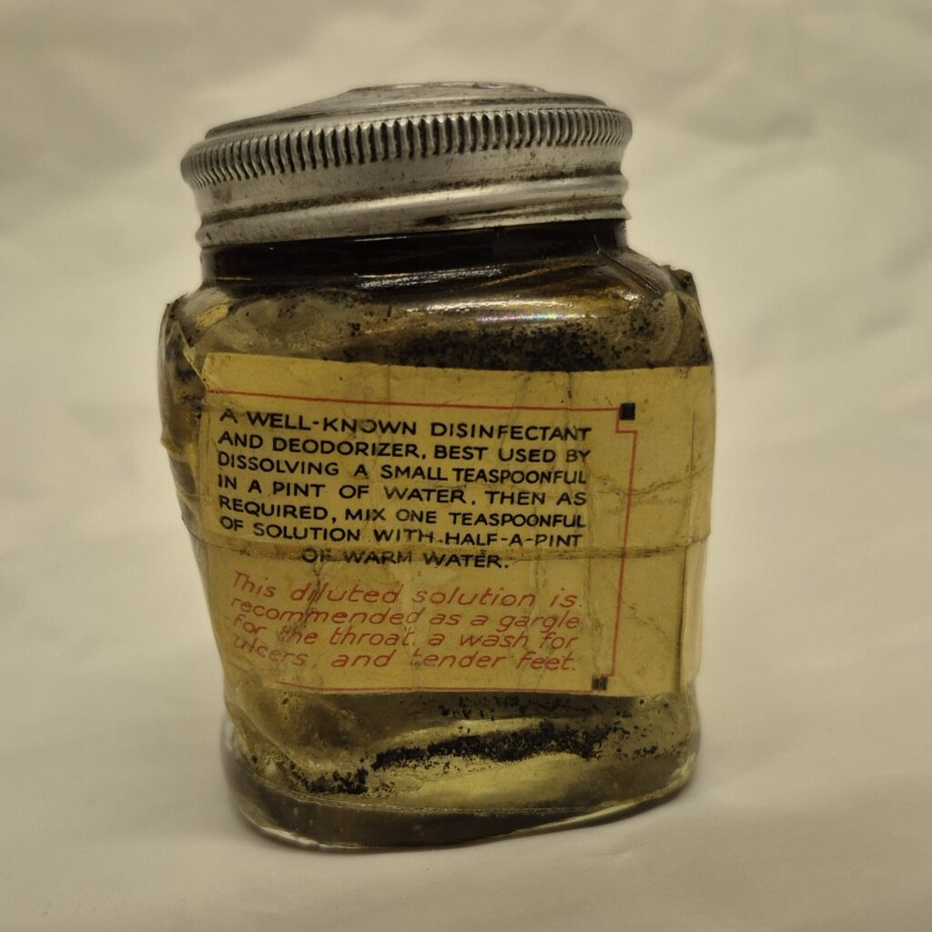 Square glass jar with metal lid. Cream label with black and then red writing