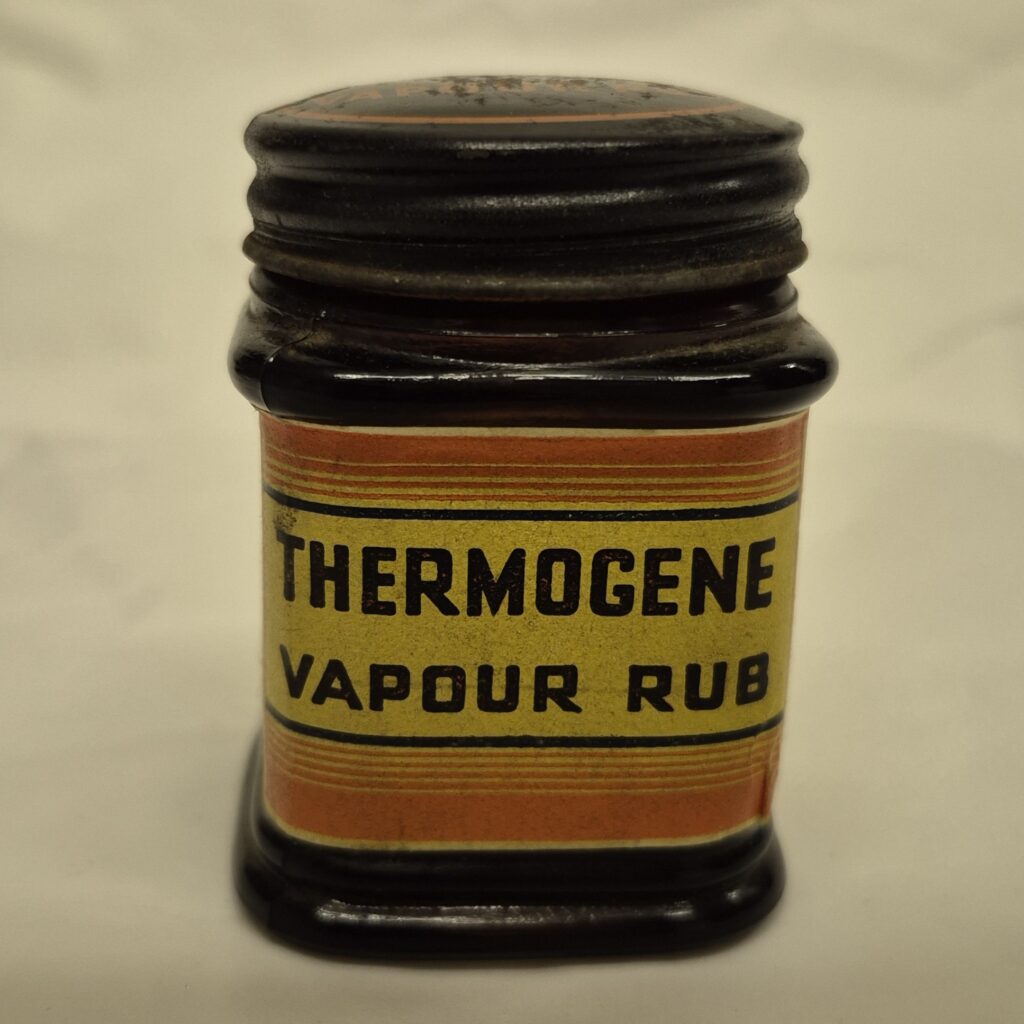 Black square jar with black metallic lid. Orange and yellow label features black text reading 'Thermogene vapor rub'