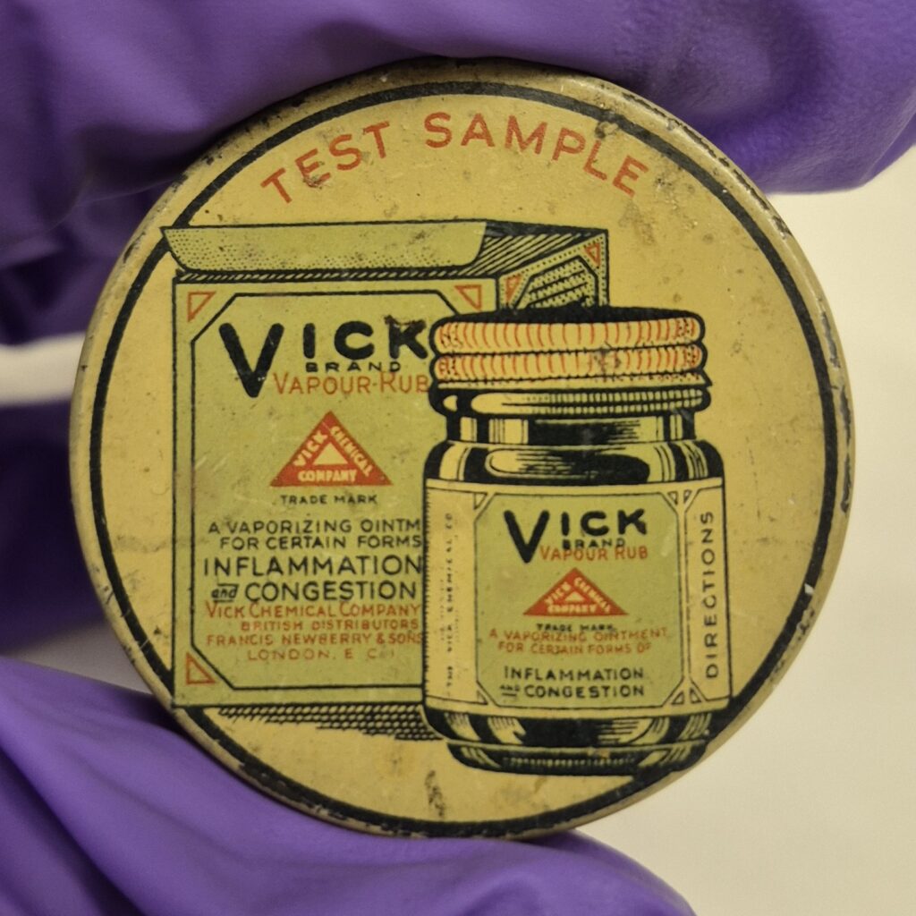 Circular cream pot with black and pale green illustration of a Vick Vapour-rub bottle and box. Above this red text reads 'Test Sample'