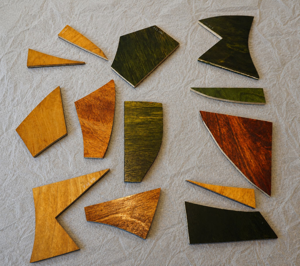 Flat lay of 13 geometric wooden puzzle pieces. The pieces vary in shape and size. 5 of the pieces are green, 1 is dark red and 7 are yellow.