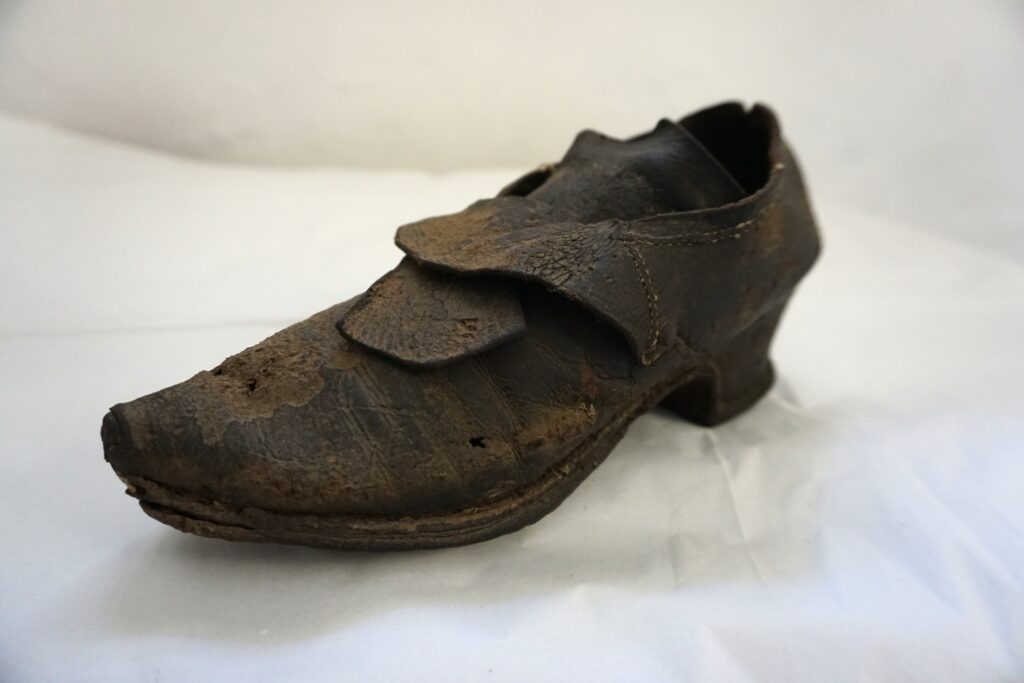 Old brown shoe in with a small heel pointed toe and two overlapping flaps over the tongue. The brown leather is worn.