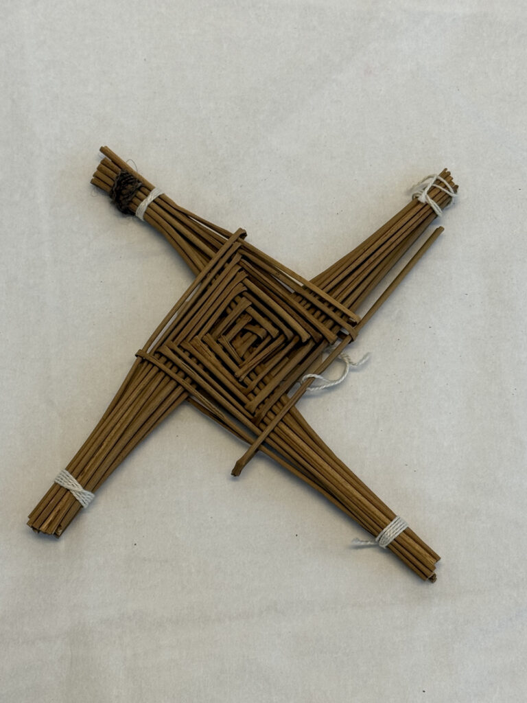 Multiple reeds of brown strands of wicker or con woven into a square at the centre with four bundles protruding from each corner and tied together at their ends by white string.