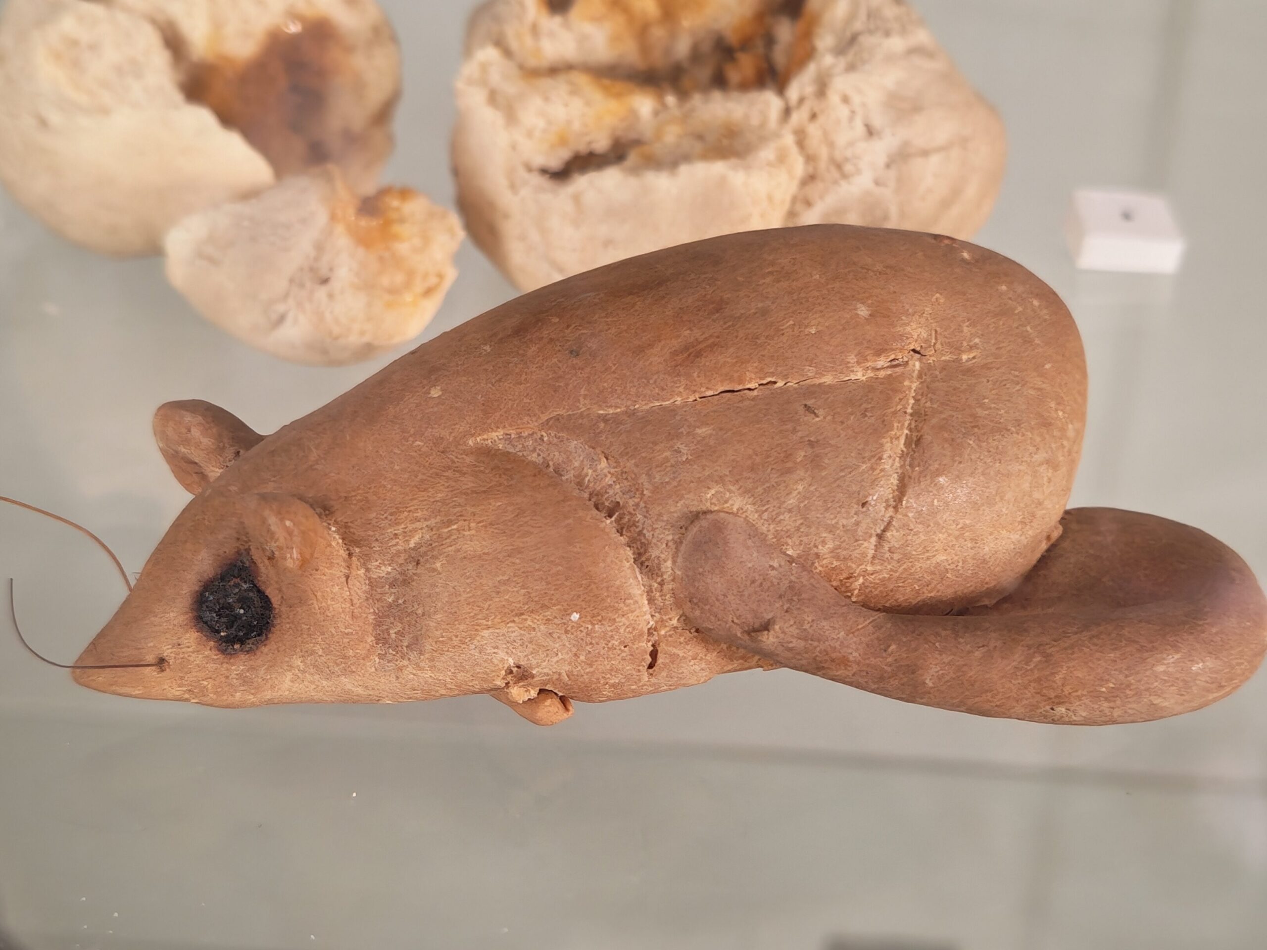 Mouse figure shaped from bead that appears brown. The mouse has black current eyes, a tail and two whiskers in the form of strings.